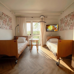 Pokój dwuosobowy z dwoma pojedynczymi łóżkami, stolikiem, telewizorem i wyjściem na balkon.